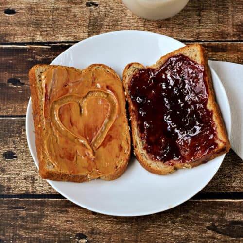 Peanut-butter-on-a-slice-of-bread-with-a-heart-in-the-center-and-jelly-on-a-second-piece-of-bread-sitting-on-a-plate.-cookingwithcurls.com-recipe-500x500